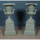 A pair of painted cast iron twin handled garden urns, raised on square bases. Height: 69cm. Piece
