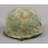 A vintage military helmet with camouflage cover and broad arrow mark to inside; stamped 21 July 1961