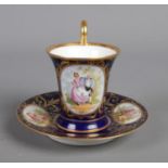 A twentieth century porcelain cup and saucer, with blue and gilt design and hand-painted panels