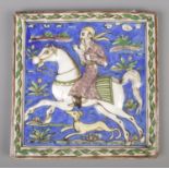 A 19th century Persian glazed tile. Painted with a rider on horse back and hound. 21cm x 21cm.