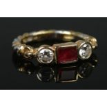 An 18ct yellow and white gold ruby and diamond ring. The central square cut ruby flanked by two