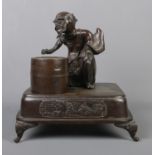 A Japanese bronze desk stand formed as a seated man and a barrel raised on square plinth with