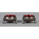 A pair of George III silver salts with red glass liners and raised on three scrolled feet. Assayed