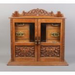 An oak smokers cabinet featuring carved detailing to doors and pediment and beveled glass panels.