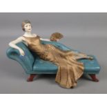 A Coalport figure of a young maiden reclining on a chaise lounge. Titled 'Penny'.