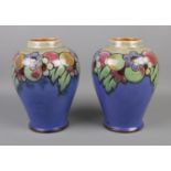 A pair of Royal Doulton vases featuring purple/blue glaze and floral borders. Approx. 21cm tall.