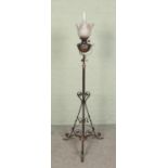 A wrought iron standard oil lamp with glass shade and adjustable stem