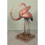 A cast metal garden ornament in the form of two standing cranes, on naturalistic base attached to