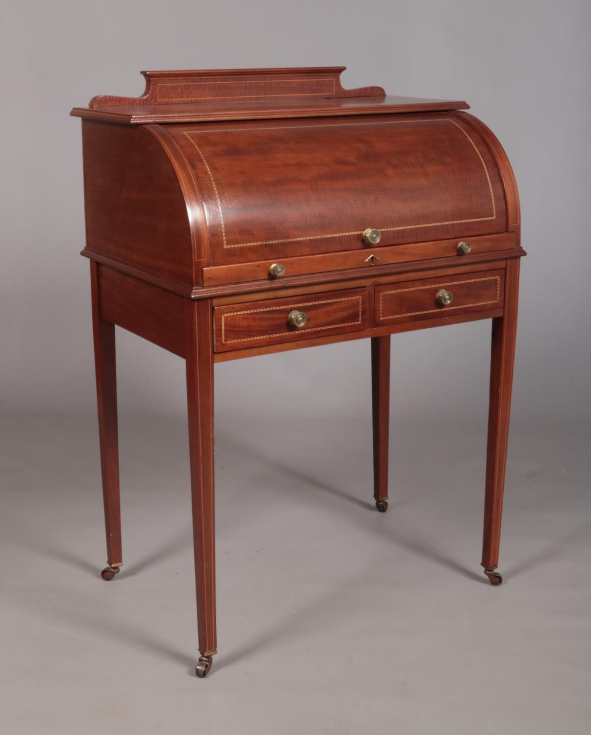 An Edwardian mahogany cylinder desk, having fitted interior, tapering supports and strung inlay.