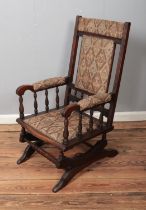 A mahogany American style rocking chair with upholstered seat and backrest and turned arm supports.