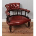 A red leather captains chair with spindle back on turned legs and brass castors