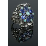 An Arts & Crafts silver ring of floral design, set with sapphire coloured and opal stones. Size P.