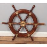 A wooden ships wheel with brass mounted hooks.
