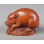 A hand carved hardwood netsuke of a pig / boar laying on a bed of leaves, signed to base.