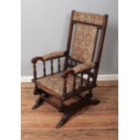 A mahogany American style rocking chair with upholstered seat and backrest and turned arm supports.