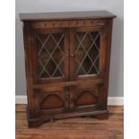An oak priory style bookcase cabinet with leaded glass doors above a pair of carved panel doors.