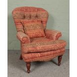 A deep buttoned spoon back armchair, with red and green patterned upholstery and turned front