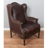 A modern leather wingback armchair, with studded back and wings, padded arms and turned reeded feet.