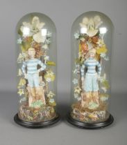 A pair of porcelain figures, formed as boy and girl in striped clothing surrounded by a composite