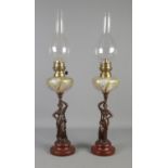A pair of Art Nouveau style oil lamps, with painted glass reservoirs and figures raised on turned