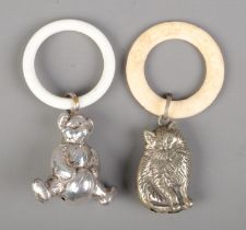 Two white metal babies rattles in the form of a teddy bear and a cat.