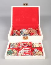 A cream hinged jewellery box containing an assortment of costume jewellery, to include paste set
