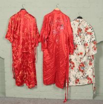 Three Japanese silk kimonos. Two red and one cream with floral design.
