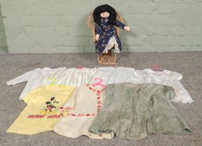 A Papier Mache doll sat in a small cane chair, together with a collection of dolls clothes.