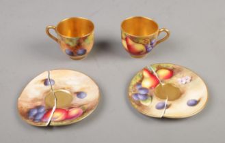 A pair of Royal Worcester hand painted gilt china cups and saucers decorated with fruit. Crack on
