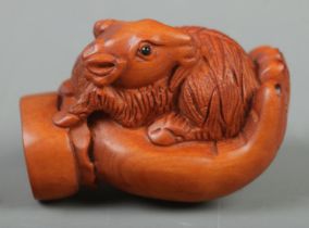 A Japanese carved Netsuke in the form of a goat on hand