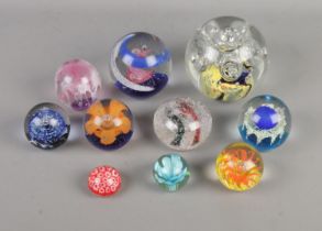 Ten glass paperweights of varying sizes to include floral examples with bubble inclusions.