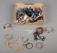 A box of assorted costume jewellery to include beaded necklaces, scrabble tile rings, bangles, etc.