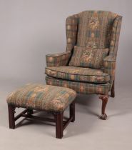 An antique style wing back arm chair raised on carved mahogany ball and claw feet, along with a foot