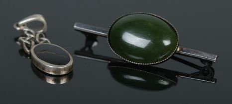 A silver brooch with single green stone with smaller silver pendant with stone.