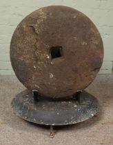 A stone mill wheel with square aperture to the centre. Mounted on base. Diameter of wheel: 53cm.