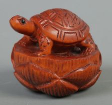 A hand carved hardwood netsuke of a turtle on lotus, signed to base.