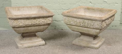A pair of concrete garden planters, with floral border decoration, raised on square stepped bases.