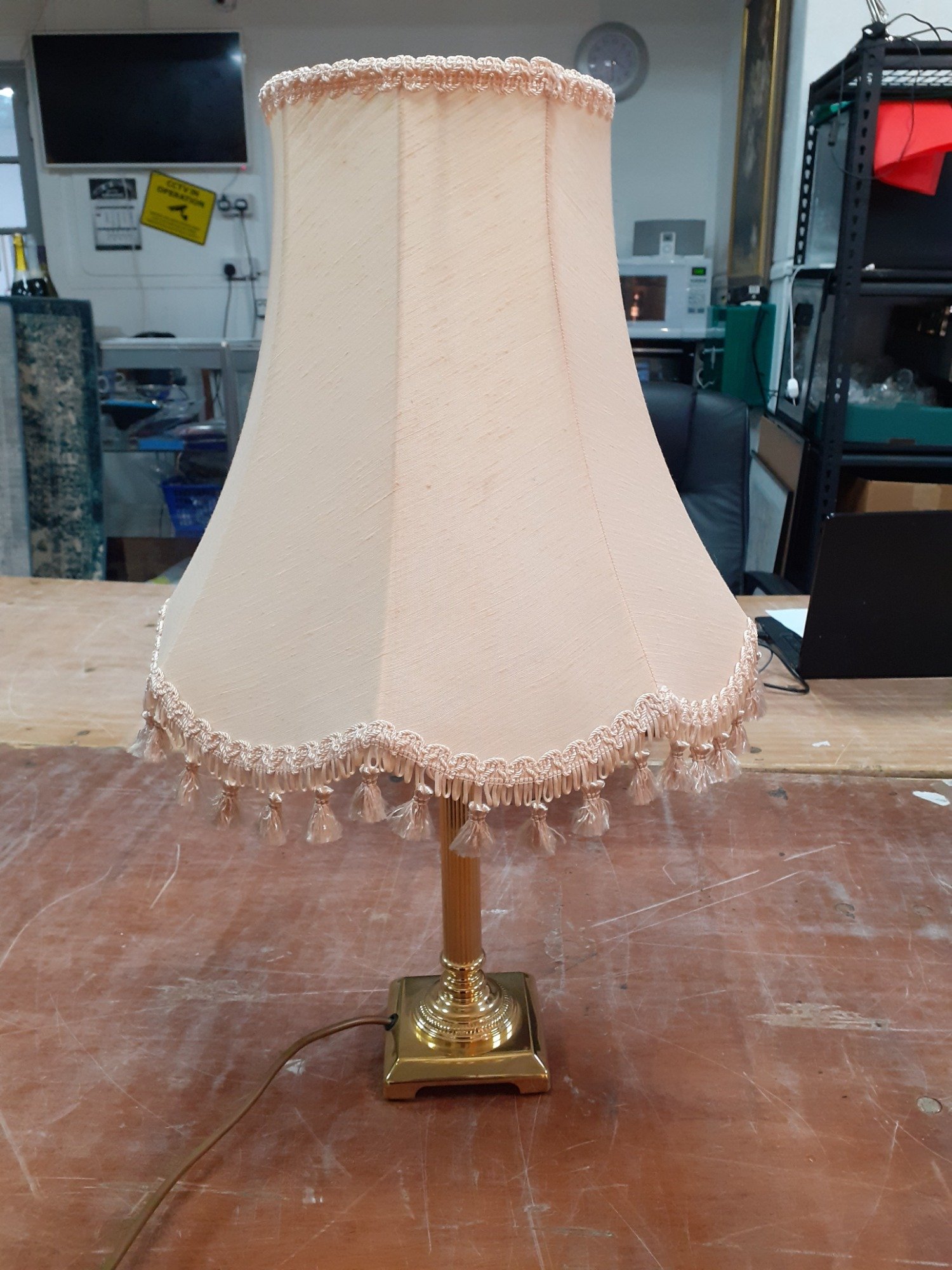 A brass table lamp with cream fringed shade standing 60cm high and in good condition.