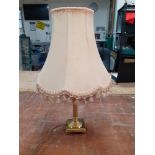 A brass table lamp with cream fringed shade standing 60cm high and in good condition.