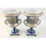 A pair of twin-handled pedestal urns with metallic feet in blue with gilt highlights each standing