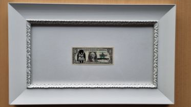 A framed stencilled DISMALAND real One Dollar bill stamped with the BANKSY chomp along with a