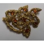 A 9ct gold pierced modernistic leaf design brooch, the textured surface set with seven brown stones,