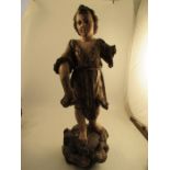 An antique carved wooden polychrome figure of a girl in a gilt dress, standing on a rocky outcrop