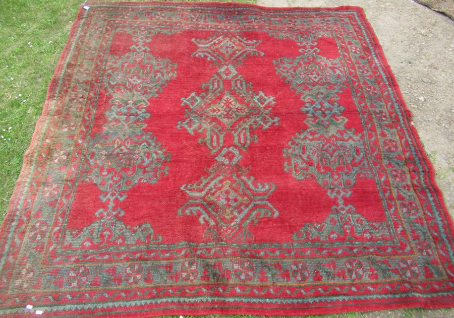 An Eastern design red ground rug, decorated with repeating symbols, 84ins x 84ins