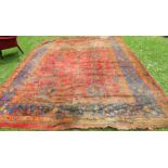 A large red ground rug, decorated with repeating motifs, 170ins x 127ins