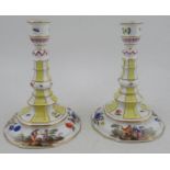 A pair of Continental porcelain candlesticks, decorated with figures and flowers, with bands of