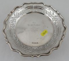A silver dish, with shaped edge, pierced border and inscription to the center, raised on three knurl