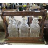 An Edwardian oak three bottle tantalus, fitted with three square glass decanters, with carved