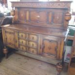 An oak sideboard, the carved upper section with cup and cover supports, the base fitted with a