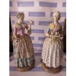 A pair of German porcelain figures, of girls, one serving the other presenting a letter, crossed